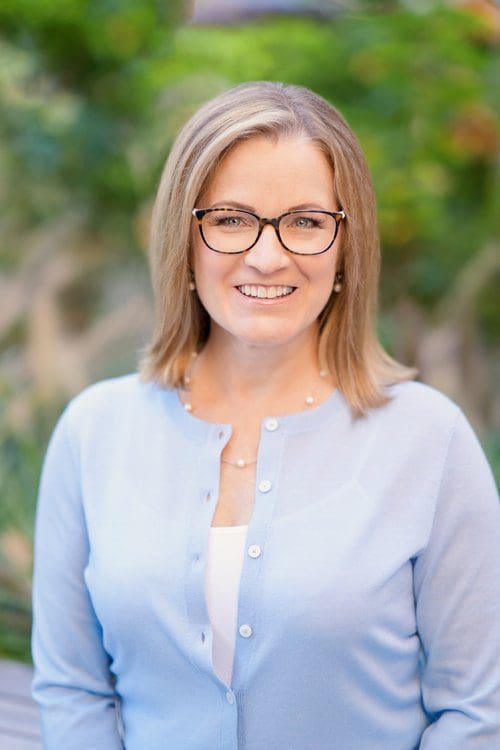 Smiling woman wearing glasses, light blue cardigan.