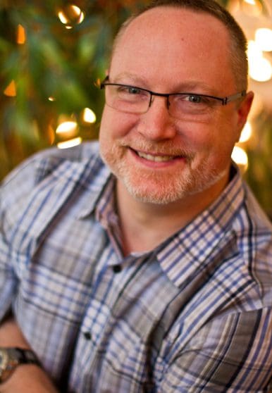 Smiling man with glasses in checkered shirt.