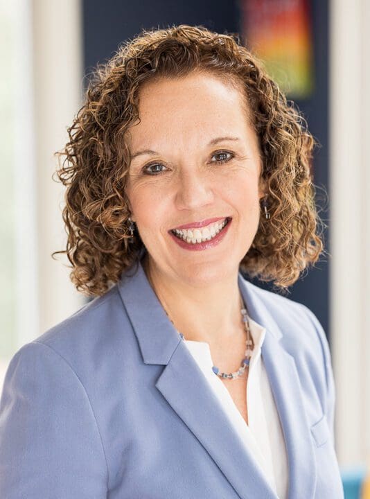 Smiling woman with curly hair in blazer.